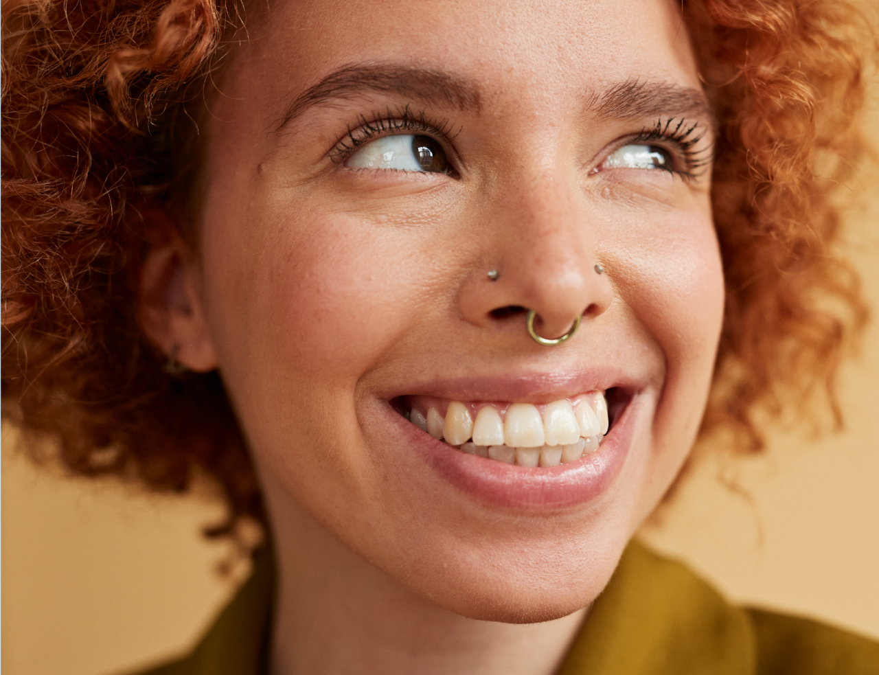 Woman with nose piercings looking up to her left and smiling