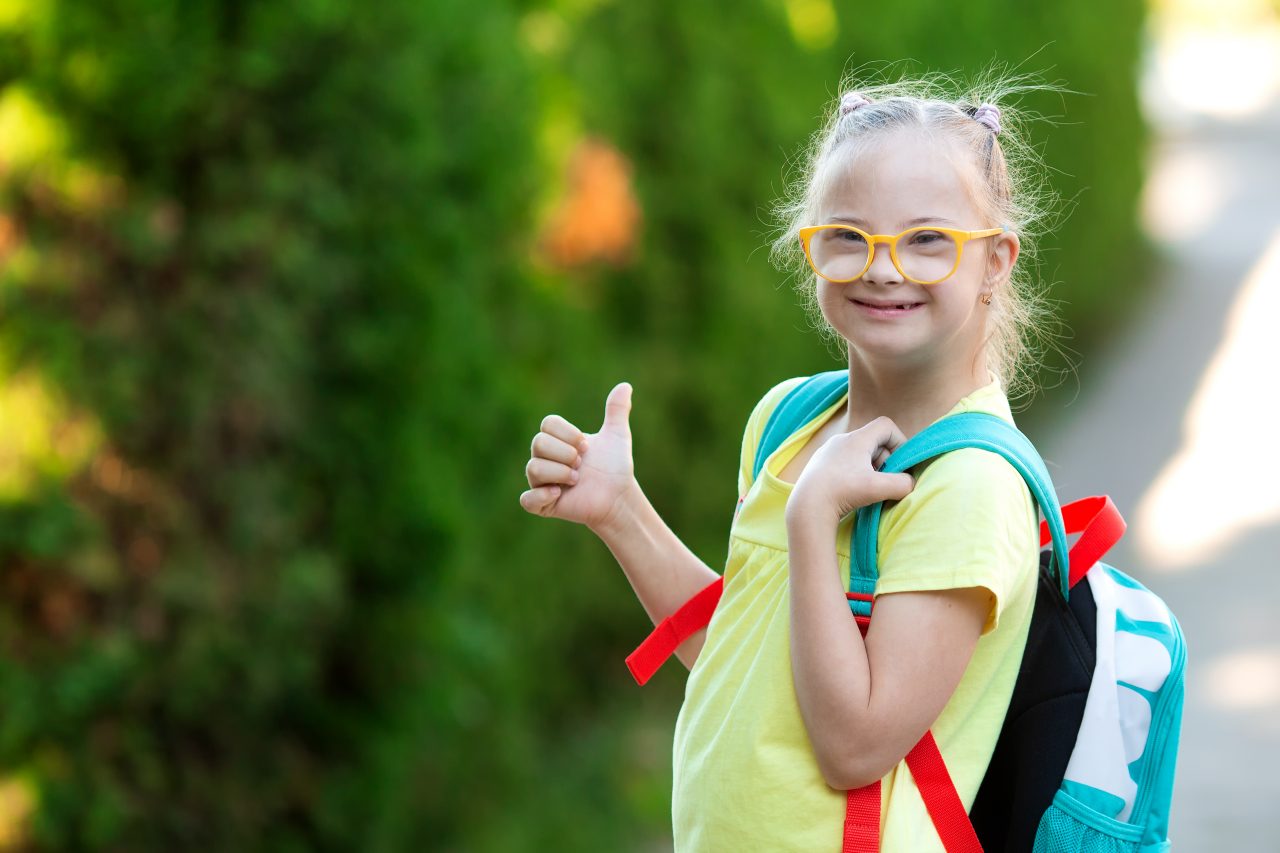 Little girl wearing backpack giving a thumbs up